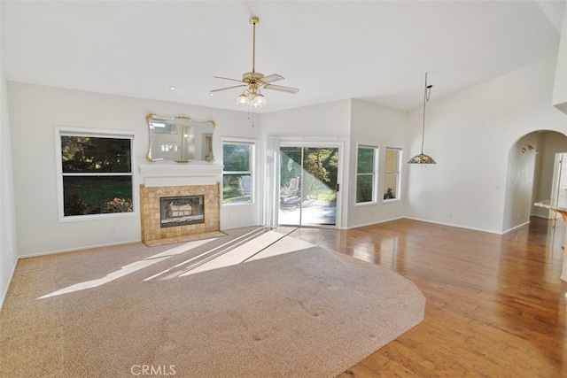 unfurnished living room featuring baseboards, arched walkways, a ceiling fan, a tile fireplace, and wood finished floors