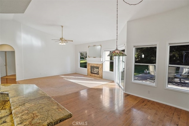 unfurnished living room with arched walkways, a ceiling fan, hardwood / wood-style flooring, a fireplace, and high vaulted ceiling