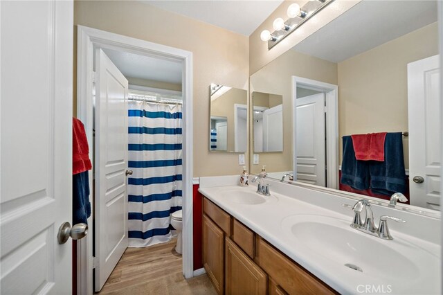 full bathroom with wood finished floors, a sink, toilet, and double vanity