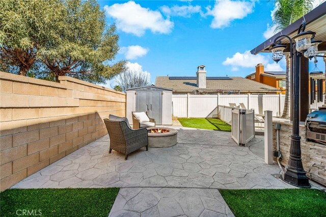 view of patio featuring a fire pit, a shed, an outbuilding, and a fenced backyard