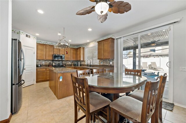 kitchen featuring stainless steel appliances, brown cabinetry, a kitchen island, and tasteful backsplash