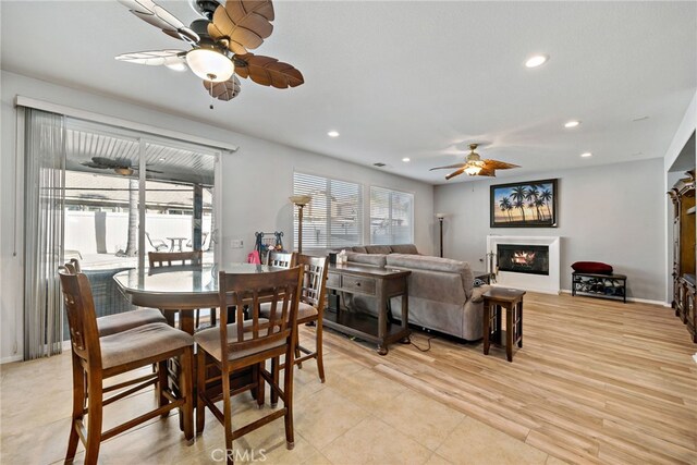 dining space with light wood finished floors, recessed lighting, a ceiling fan, a glass covered fireplace, and baseboards