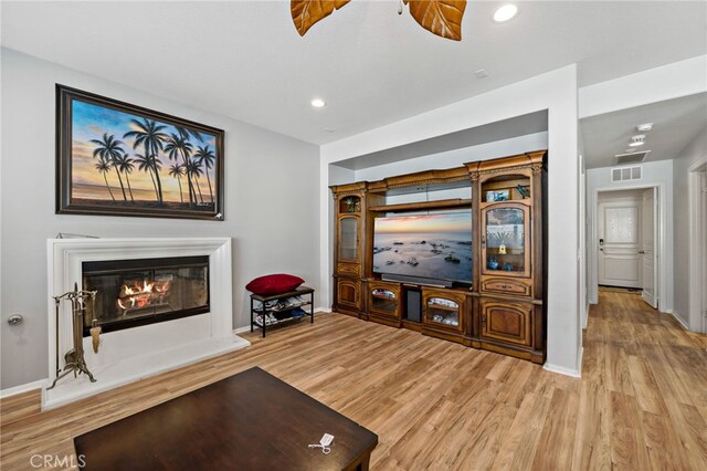 living room with light wood-style floors, a glass covered fireplace, ceiling fan, and baseboards