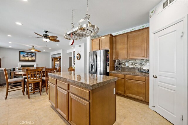 kitchen with tile countertops, a fireplace, a kitchen island, stainless steel fridge with ice dispenser, and decorative backsplash