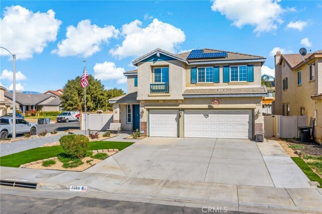 traditional-style house featuring solar panels, an attached garage, a gate, fence, and stucco siding