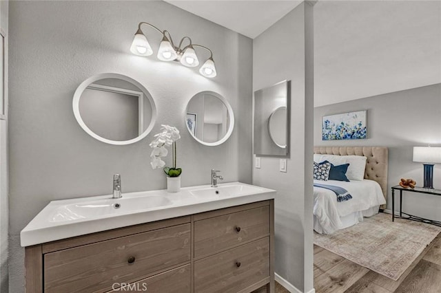 ensuite bathroom featuring double vanity, a sink, ensuite bath, and wood finished floors