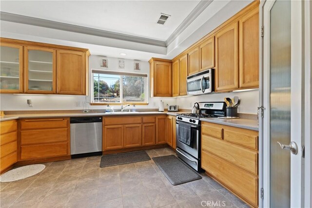 kitchen with crown molding, stainless steel appliances, visible vents, glass insert cabinets, and a sink