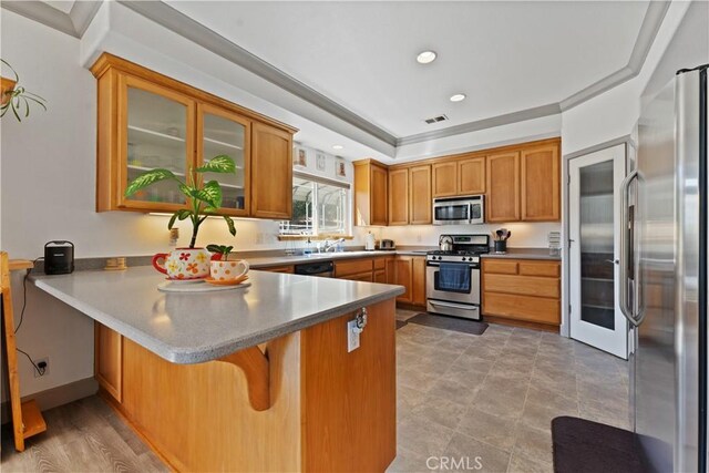 kitchen with visible vents, glass insert cabinets, brown cabinets, a peninsula, and stainless steel appliances