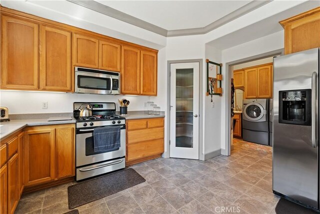 kitchen with washer and dryer, light countertops, ornamental molding, appliances with stainless steel finishes, and brown cabinetry