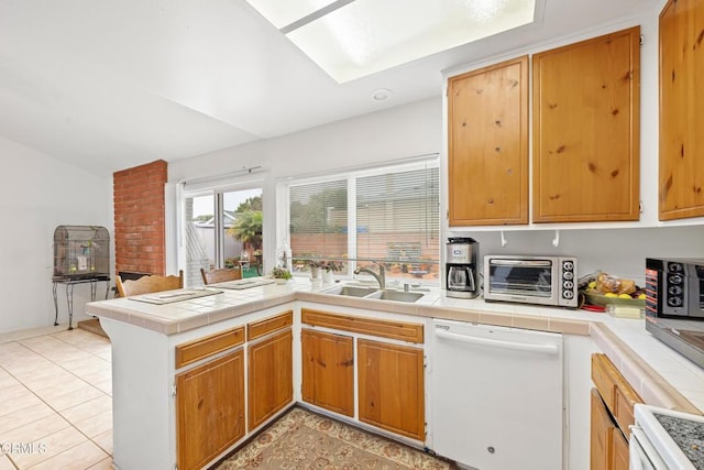 kitchen featuring a toaster, tile counters, dishwasher, a peninsula, and a sink