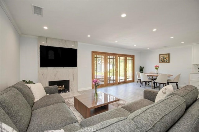 living room featuring visible vents, recessed lighting, crown molding, light wood finished floors, and a premium fireplace