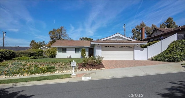 ranch-style home with fence, an attached garage, stucco siding, a front lawn, and decorative driveway