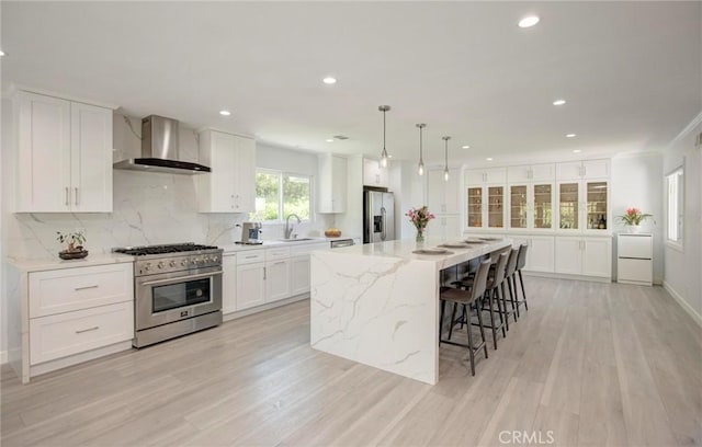 kitchen featuring light wood-type flooring, appliances with stainless steel finishes, white cabinets, wall chimney range hood, and decorative backsplash