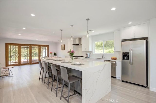 kitchen with a kitchen island, appliances with stainless steel finishes, white cabinetry, wall chimney exhaust hood, and a sink