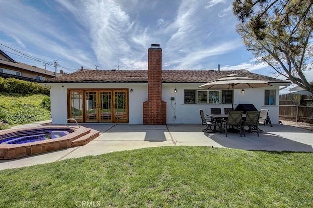 rear view of property featuring fence, stucco siding, a chimney, a patio area, and an in ground hot tub