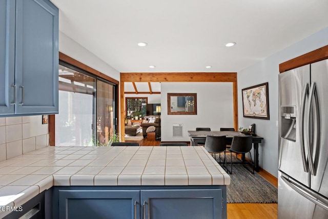 kitchen with blue cabinets, tile countertops, stainless steel fridge, a peninsula, and light wood finished floors