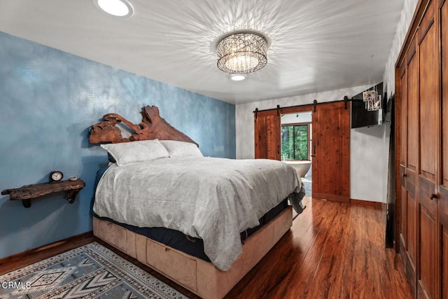 bedroom featuring an inviting chandelier, baseboards, a barn door, and wood finished floors