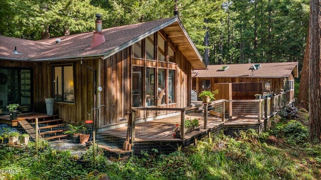 back of house with a deck, a view of trees, and a shingled roof