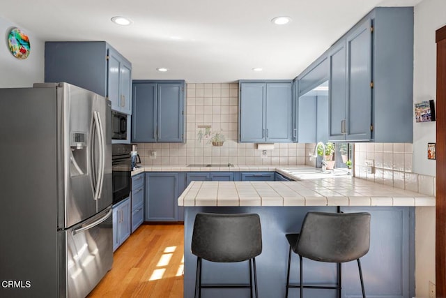 kitchen featuring a peninsula, blue cabinetry, a sink, black appliances, and light wood-style floors