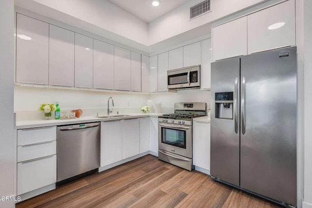 kitchen featuring wood finished floors, light countertops, white cabinets, a sink, and appliances with stainless steel finishes