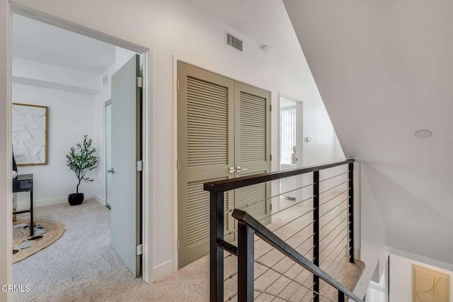hall featuring carpet floors, visible vents, an upstairs landing, and vaulted ceiling
