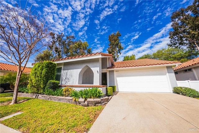 mediterranean / spanish-style house with a garage, fence, concrete driveway, and stucco siding