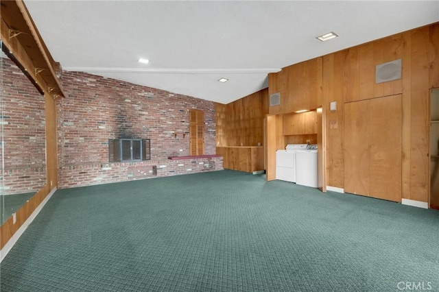 unfurnished living room with vaulted ceiling, carpet, independent washer and dryer, and wood walls