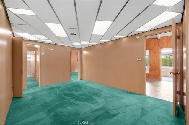 unfurnished room with light carpet, wooden walls, visible vents, and a drop ceiling