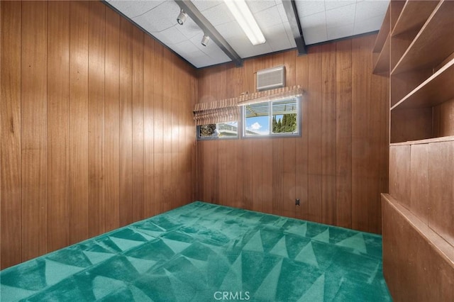 empty room featuring rail lighting, wooden walls, beamed ceiling, and carpet flooring