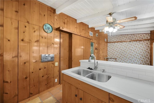 kitchen with beam ceiling, visible vents, a ceiling fan, a sink, and wooden walls