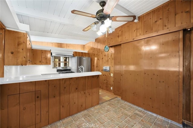 kitchen featuring appliances with stainless steel finishes, brown cabinets, beamed ceiling, a peninsula, and wood walls