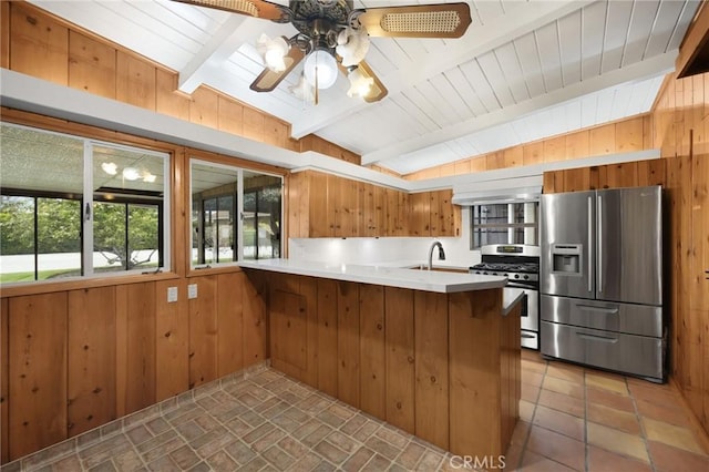 kitchen featuring light countertops, appliances with stainless steel finishes, brown cabinetry, wood walls, and a peninsula