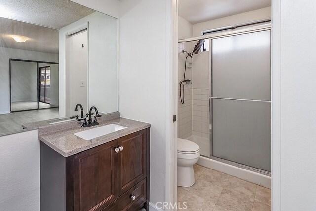 bathroom with toilet, a stall shower, vanity, a textured ceiling, and tile patterned floors