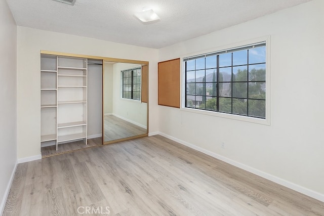 unfurnished bedroom with a closet, baseboards, light wood-style flooring, and a textured ceiling