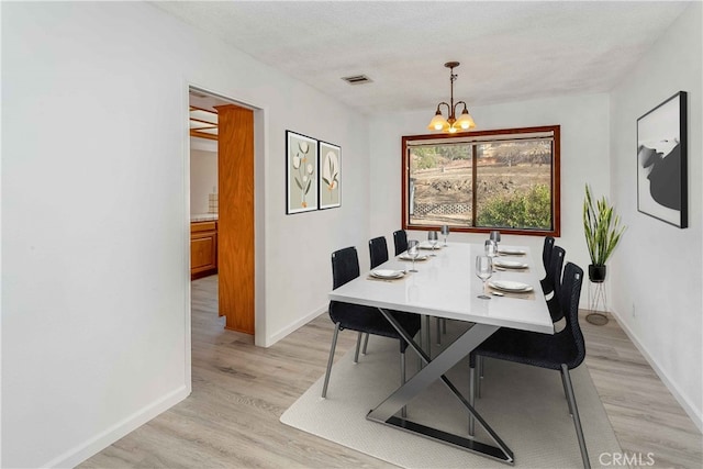 dining space with visible vents, light wood-style flooring, an inviting chandelier, a textured ceiling, and baseboards