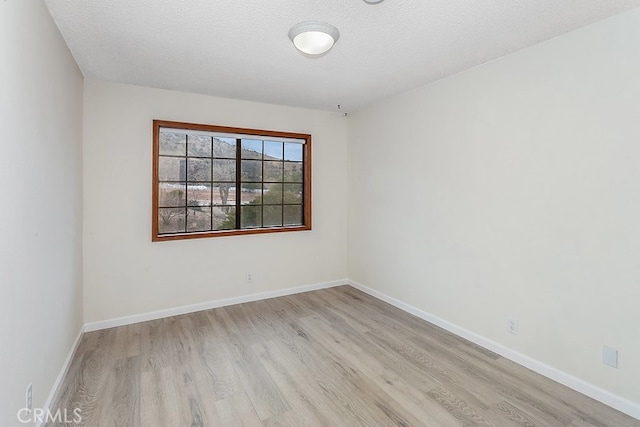 spare room featuring light wood finished floors, baseboards, and a textured ceiling