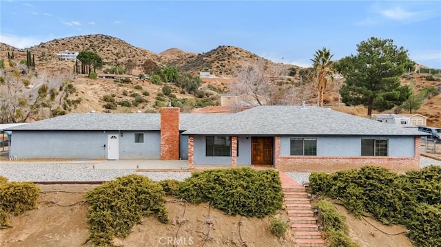 ranch-style house featuring a mountain view, brick siding, a shingled roof, stairway, and a chimney