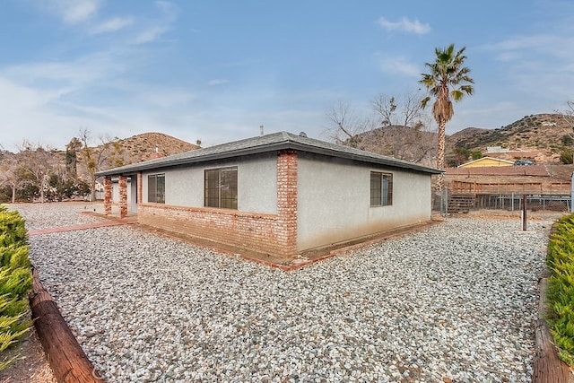 view of side of home with brick siding, fence, a mountain view, and stucco siding