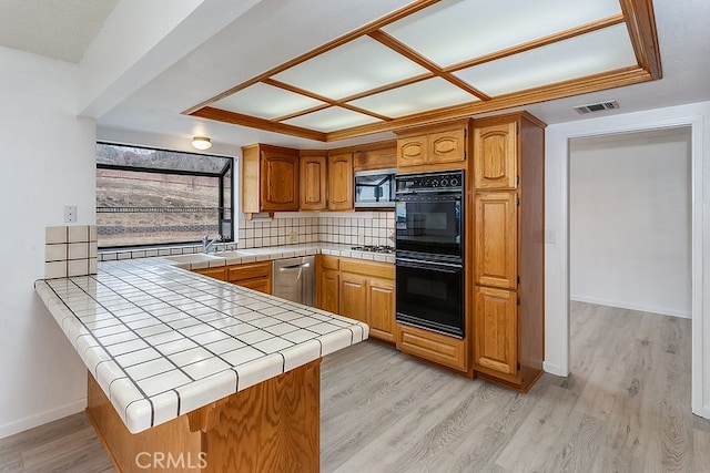 kitchen featuring visible vents, tile counters, light wood-style flooring, a peninsula, and stainless steel appliances