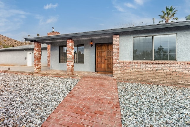 view of front of property with brick siding, a chimney, and stucco siding