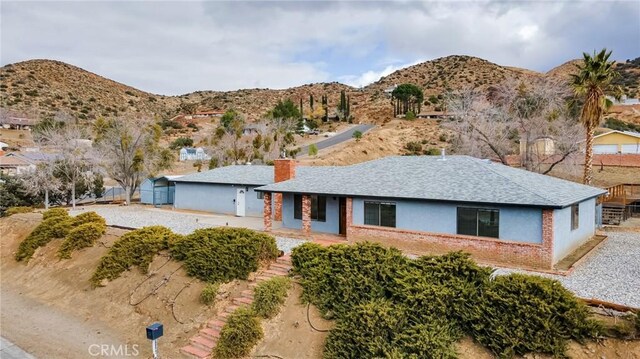 ranch-style house featuring a mountain view, brick siding, fence, roof with shingles, and a chimney