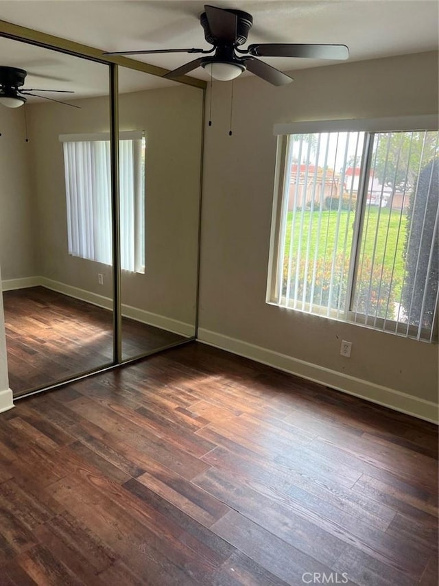 unfurnished bedroom with ceiling fan, dark wood-style flooring, a closet, and baseboards