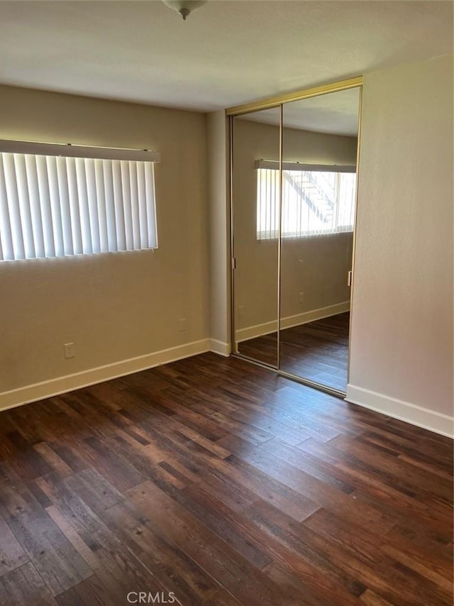 unfurnished bedroom featuring a closet, wood-type flooring, and baseboards