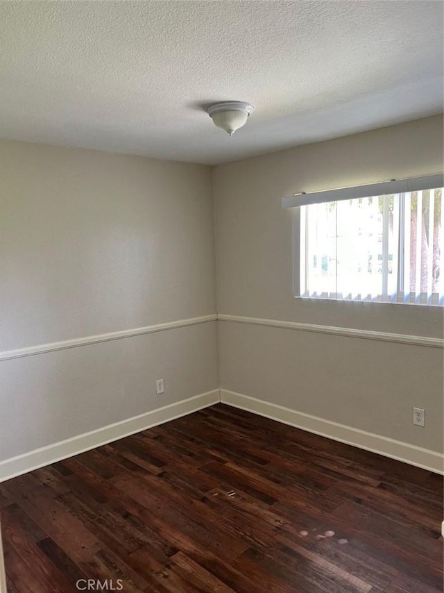 empty room featuring baseboards, dark wood finished floors, and a textured ceiling