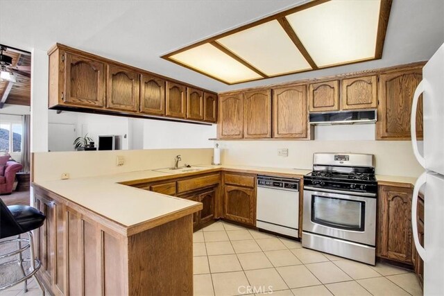 kitchen featuring white appliances, brown cabinetry, a peninsula, under cabinet range hood, and a sink