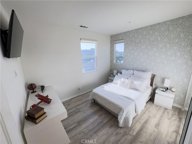 bedroom featuring visible vents, wallpapered walls, baseboards, and wood finished floors