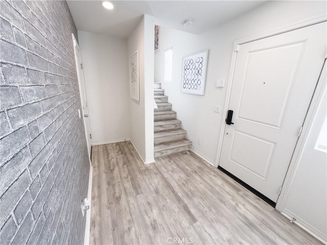 foyer entrance featuring brick wall, baseboards, light wood-type flooring, stairs, and recessed lighting