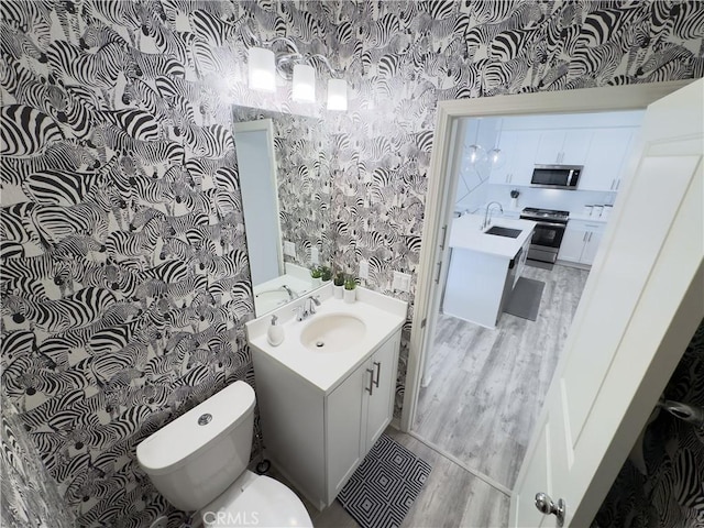 bathroom with wallpapered walls, wood finished floors, toilet, and vanity