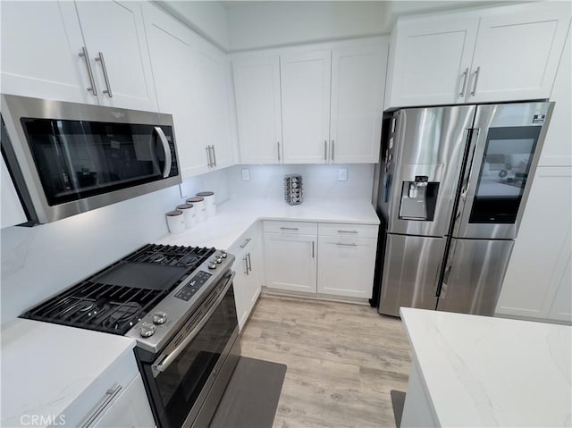 kitchen featuring white cabinets, light stone counters, light wood-type flooring, and stainless steel appliances