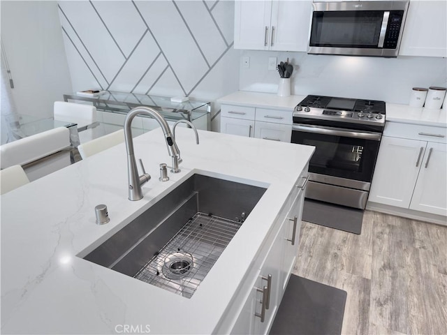 kitchen with light wood finished floors, white cabinetry, stainless steel appliances, and a sink